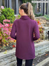 Miik model Johanna (5’6”, xsmall) standing with her back towards the camera showing the back of Miik's 		Ashanti long sleeve cowl neck pocket tunic