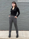 Woman standing in front of a brick wall wearing Miik's Asia mid-rise slim pant in granite along with a botton up shirt in black