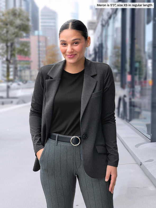 A close up shot of Miik model Meron (5'3", xsmall) smiling wearing Miik's Asia mid-rise slim pant in granite wide pinstripe with a charcoal blazer and a black top and belt 