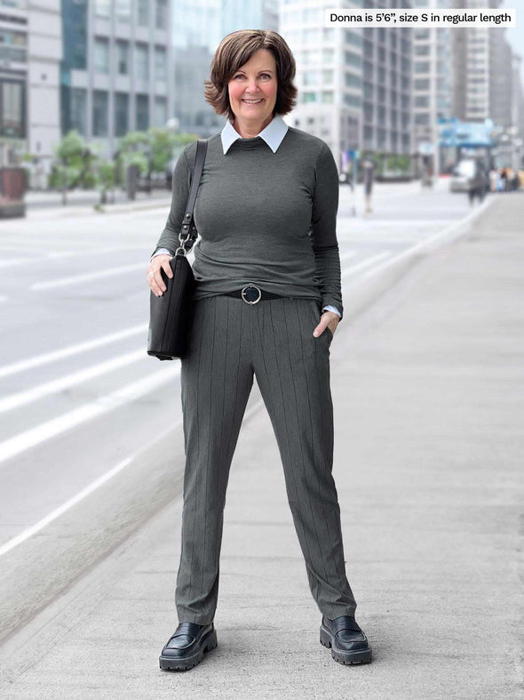 Miik founder Donna (5'6", small) smiling wearing Miik's Asia mid-rise slim pant in granite wide pinstripe along with a turtleneck tup in granite and a collared white shirt 