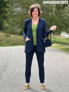 Miik founder Donna (5'6", small) smiling wearing Miik's Asia mid-rise slim pant navy in regular length with a cardigan in the same colour and a green moss tank top 