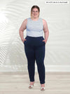 Miik model Bri (5'5", xlarge) smiling wearing Miik's Asia mid-rise slim pant in navy short length with a striped tank top