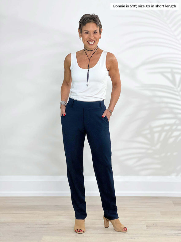 Miik model Bonnie (5'0", xsmall, petite) smiling wearing Miik's Asia mid-rise slim pant navy in short length with a white tank top 