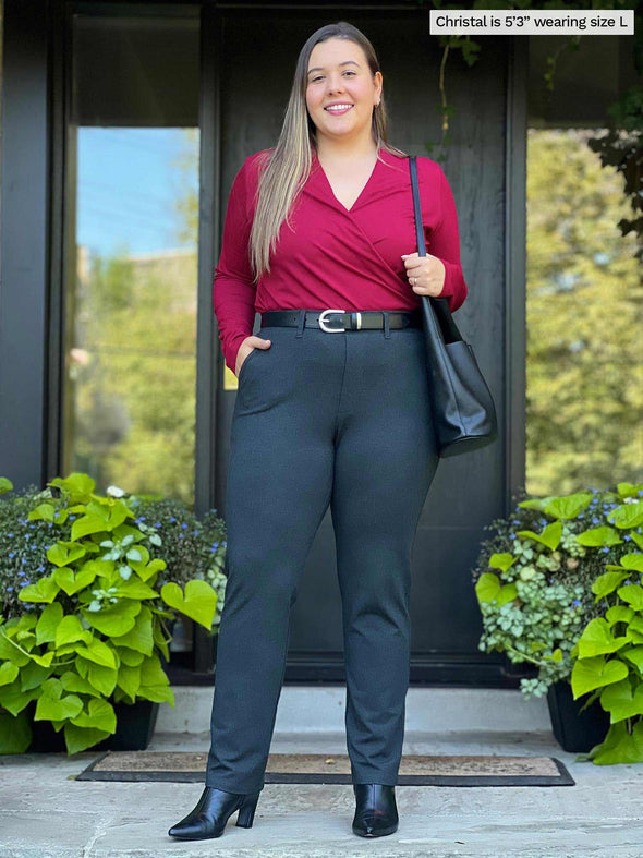 Woman standing in front of a house wearing Miik's Asia mid-rise slim pant in charcoal with a red top.