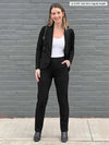 Woman standing in front of a brick wall wearing Miik's Asia mid-rise slim pant in black with a matching colour blazer and a white tank
