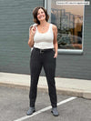Woman standing in a parking lot wearing an oatmeal tank top along with Miik's Asia mid-rise slim pant in charcoal pinstripe with a black belt and and oatmeal blazer on her shoulders