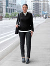 Miik model Meron (5'3", xsmall) smiling wearing Miik's Asia mid-rise slim pant in charcoal wide pinstripe with a black top on top of a turtleneck top in oatmeal