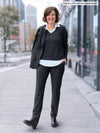 Miik founder Donna (5'6", small) smiling wearing a collared white shirt under a charcoal v-neck long sleeve top along with Miik's Asia mid-rise slim pant in charcoal wide pinstripe 