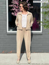 Miik founder Donna (five feet six, size small) standing in front of a window looking away wearing a matching casual suit in wheat: Miik's Ayesha zipped jacket and Nadia scuba pants along with a tee in cobblestone print