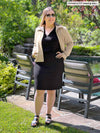 Miik model Christal (five feet three, large) standing in front of a pool looking away wearing Miik's Ayesha zipped jacket in wheat with a top and pencil skirt in black