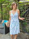 Woman standing in backyard smiling while wearing Miik's benton wrap dress in blue leaf pattern