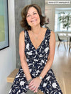 Miik founder Donna (five feet six, small) smiling while seating in her living room wearing Miik's Blakely faux-wrap dressy jumpsuit in blossom print