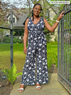 Miik model Pat (five feet eight, large) standing next to a backyard gate wearing Miik's Blakely faux-wrap dressy jumpsuit in blossom print