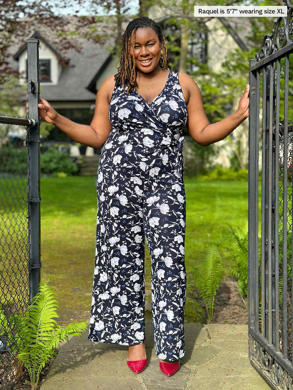 Miik model Raquel (five feet seven, xlarge) smiling in a backyard wearing Miik's Blakely faux-wrap dressy jumpsuit in blossom print