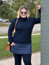 Woman standing next to a brick wall and smiling wearing Miik's Brooklin mock neck pocket tunic in navy/navy melange with a matching colour legging
