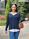 Miik model Yasmine (5'0", xsmall, petite) smiling wearing Miik's Carson collared faux-layer shirt in navy with jeans and a brown purse 