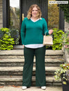 Miik model Bri (5'5", xlarge) smiling while standing on a entry door stairs wearing Miik's Carson collared faux-layer shirt in jade melange along with a flare pant in green pine