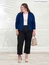 Miik model Bri (5'5", xlarge) smiling and looking away wearing Miik's Cassandra pull-n pocket capri pant in black along with a natural tank and a cropped ink blue blazer 