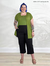 Miik model Kaitlin (5'9", xxlarge) smiling wearing Miik's Cassandra pull-on pocket capri pant in black with a green moss cardigan and top 