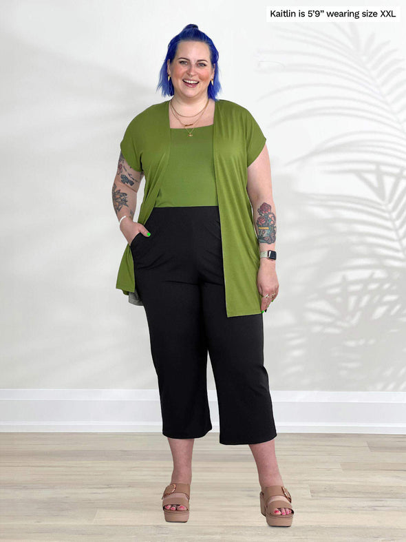 Miik model Kaitlin (5'9", xxlarge) smiling wearing Miik's Cassandra pull-on pocket capri pant in black with a green moss cardigan and top 