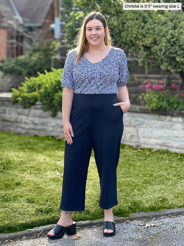 Miik model Christal (5'3", large) smiling wearing a printed blue top tucked in Miik's Cassandra pull-on pocket capri pant in navy