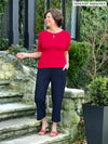 Miik founder Donna (5'6", small) smiling and looking away wearing Miik's Cassandra pull-on pocket capri pant in navy with a poppy red top