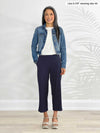 Miik model Lisa (5'6", xsmall) smiling while standing in front of a white wall wearing a white tee, a denim jacket and Miik's Cassandra pull-on pocket capri pant in navy 
