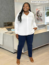 Miik model plus size Kimesha (5'8", 3x) smiling, looking away while standing in a living room wearing a white collared shirt with Miik's Christal pull-on pintuck ankle pant in navy