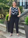 Miik model Christal (5'3", large) smiling while looking up wearing a printed tank top tucked in Miik's Christal pull-on pintuck ankle pant in black in the short length