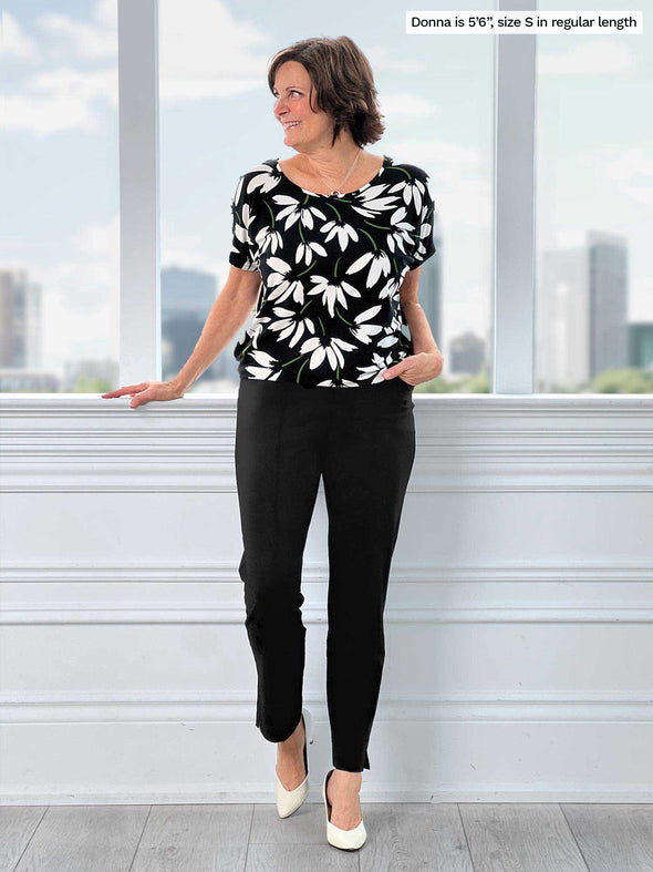 Miik founder Donna (5'6", small) smiling and looking away in a studio wearing a printed top with Miik's Christal pull-on pintuck ankle pant in black in the regular length
