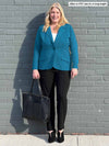 Woman standing in front of a wall wearing Miik's Christal pull-on pintuck ankle pant in black with a blue blazer.