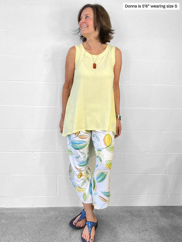 Woman standing in front of a wall wearing Miik's Dalya high-low flowy tunic tank in yellow with leaf pattern pants.