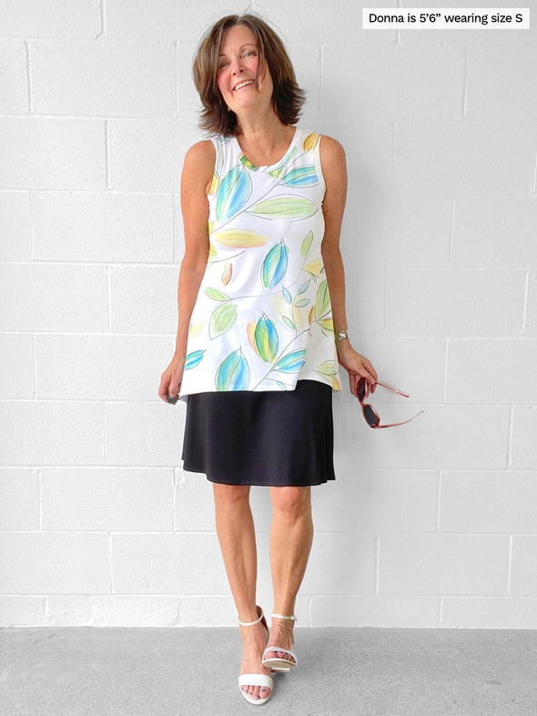 Woman standing in front of a wall wearing Miik's Dalya high-low flowy tunic tank in leaf pattern with a black skirt.