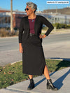 Woman standing on the street wearing Miik's Devon pocket midi skirt in black with a burgundy top and a black cardigan.