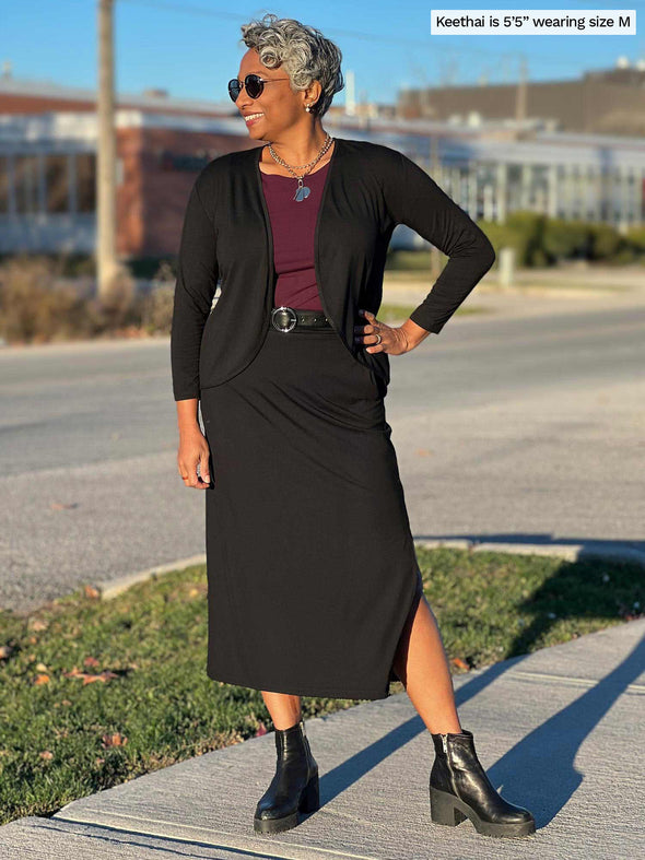 Woman standing on the street wearing Miik's Devon pocket midi skirt in black with a burgundy top and a black cardigan.