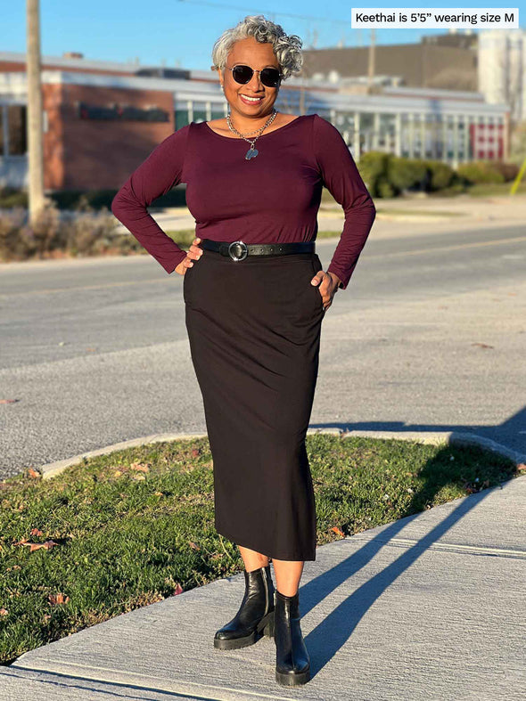 Woman standing on the street wearing Miik's Devon pocket midi skirt in black with a burgundy top.
