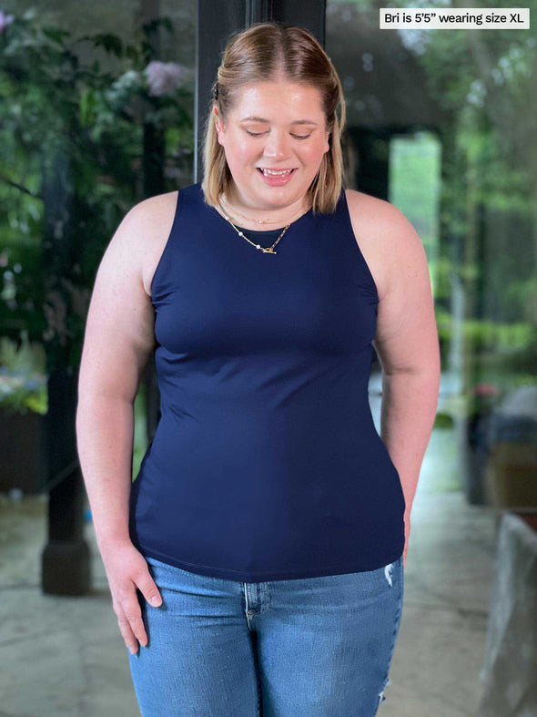 Miik model Bri (five feet five, xlarge) smiling and looking down wearing Miik's Dolly high neck tank top in navy untucked with jeans 