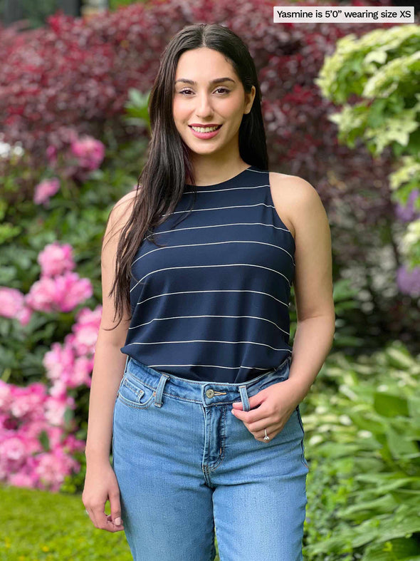 Miik model Yasmine (five feet tall, xsmall, petite) smiling wearing Miik's Dolly high neck tank top in navy wide pinstripe tucked with jeans 