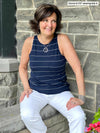 Miik founder Donna (five feet six, small) sitting next to a brick wall, smiling and looking away wearing Miik's Dolly high neck tank top in navy wide pinstripe with white jeans 