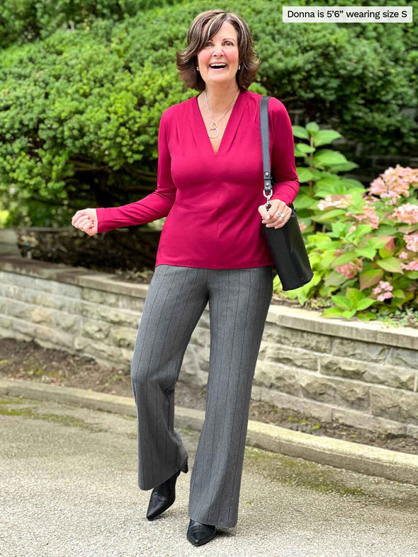 Miik founder Donna (5'6 - small) laughing wearing a pinstripe granite flare pant along with Miik's Dua v-neck long sleeve blouse in bordeaux with black shoes and purse 