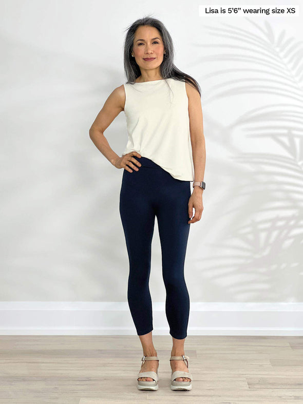 Miik model Lisa (5'6", xsmall) standing in front of a white wall wearing a capri legging pant in navy with Miik's Eline reversible shelf bra tank in natural