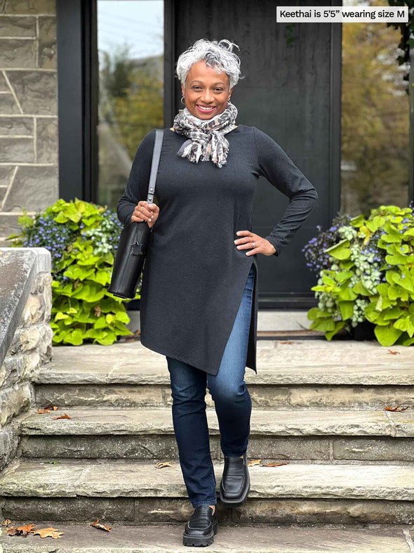 Miik model Keethai (5'5", medium) going down stairs and smiling wearing Miik's Elsie asymmetrical long sleeve tunic in charcoal with jeans and a animal print scarf