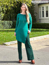 Miik model Johanna (5'6", xsmall) smiling wearing Miik's Elsie asymmetrical long sleeve tunic in jade melange along with a flare pant in green pine