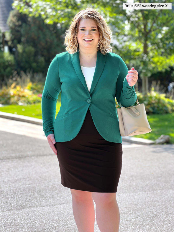 Miik model Bri (size XL, 5 foot 5) wearing the Emily professional blazer buttoned in jade melange green over a white tank top tucked into a corporate pencil skirt.