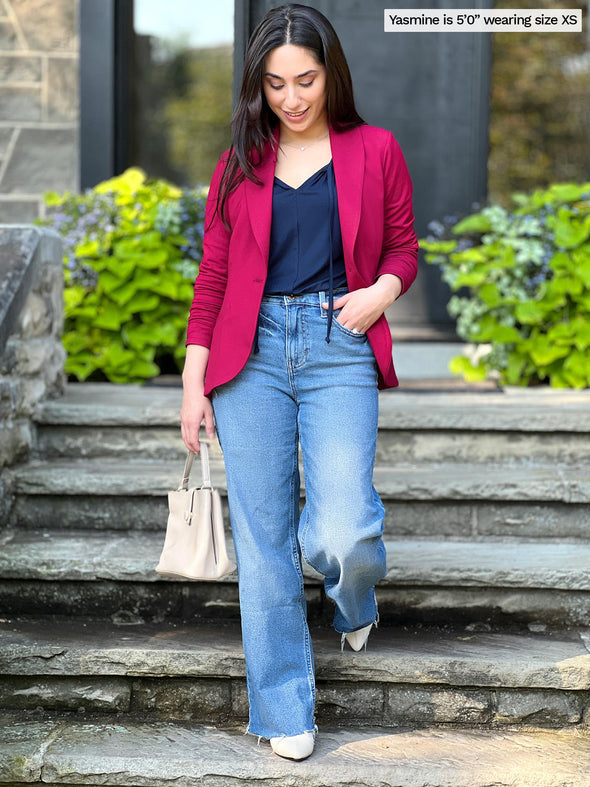 Miik model Yasmine (size XS, 5 feet) wearing the Emily soft blazer for women unbuttoned in bordeaux red over a navy top tucked into jeans.
