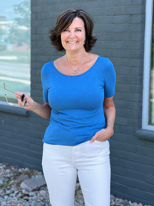 Miik founder Donna (five feet six, small) smiling in front of a brick wall wearing Miik's Emmy reversible half sleeve top in cobalt melange with a white jeans