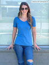 Miik model Johanna (five feet six, xsmall) standing in front of a window smiling wearing Miik's Emmy reversible half sleeve top in cobalt melange with a ripped jeans and sunglasses 