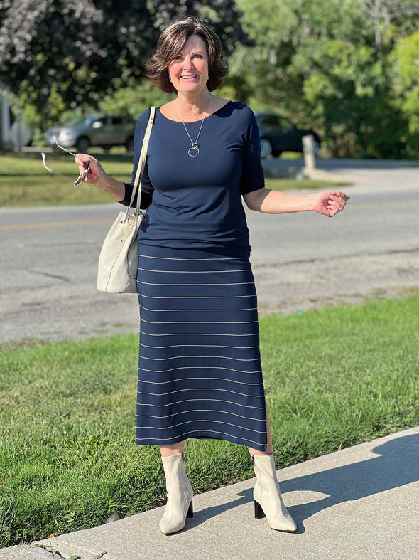 Miik founder Donna (five feet six, small) smiling wearing Miik's Hilden ballet top in navy along with a midi skirt in the same colour but pinstripe, boots and a shoulders purse