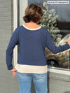 Woman standing with her back towards the camera showing the back of Miik's Geneva two-tone crew neck top in navy melange/oatmeal