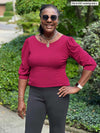 Miik model Pat (five feet eight, large) smiling while wearing Miik's Gigi reversible puff sleeve blouse in bordeaux with a graphite pant and sunglasses 